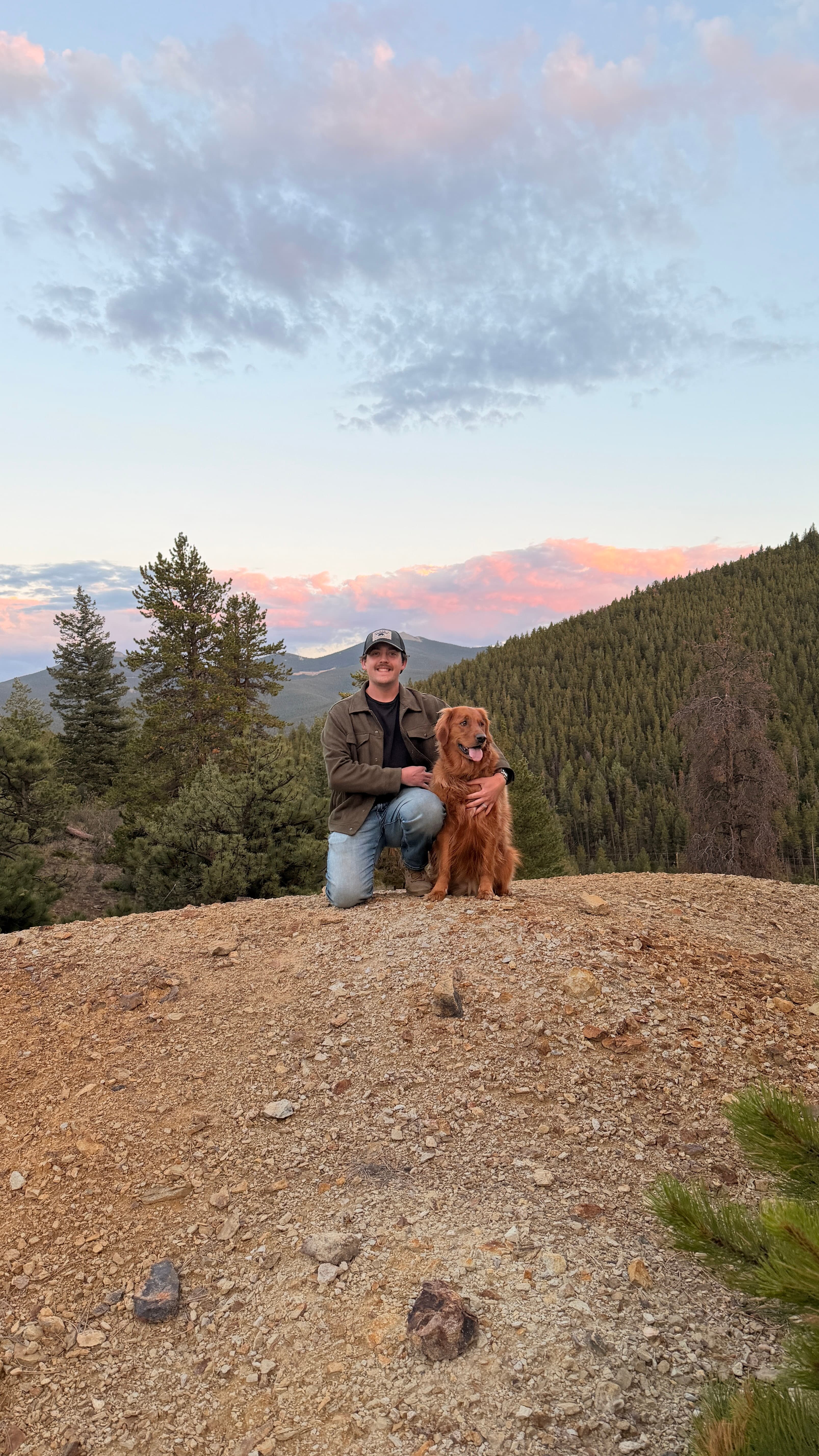Traceton kneeling beside his dog in the Colorado mountains